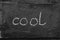 The word cool written with chalk on black stone.