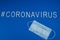 The word coronavirus laid with white letters on classic blue background. Respiratory protection mask next to the word #coronavirus