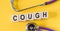 Word COUGH building from wooden cubes on yellow desk with stethoscope