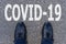Word COVID-19 written on asphalt with shoes, concept background