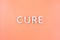 The word cure laid with thick aluminium letters on light orange pastel color background