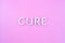 The word cure laid with thick aluminium letters on pink background