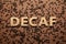 Word Decaf made of wooden letters on brown background with coffee beans, flat lay