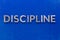 The word discipline laid with silver metal characters on blue painted wooden board in central flat lay composition