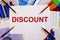The word DISCOUNT is written on a white background in red font near pens, pencils and graphics. Financial concept