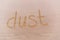 Word `Dust` written on dusty wooden surface