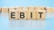 word ebit made with wood building blocks. blue background. business concept