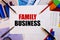 The word FAMILY BUSINESS is written on a white background near colored graphs, pens and pencils. Business concept