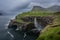 Word famous Mulafossur waterfall falling from the cliff into the ocean in the strong wing. Cloudy, windy  weather in Faroe Islands