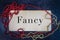 The word fancy painted on wooden board with red and gold beaded necklaces flat lay