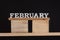 Word February made of wooden letters on wooden stand. Black background. Front view