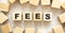 The word FEES consists of wooden cubes with letters, top view on a light background