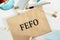 The word FEFO - abbreviation of first expired first out on crafted envelope lying on the desk with office tools