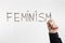 Word FEMINISM written on glass board with female hand