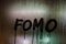 word FOMO - Fear Of Missing Out - handwritten on night wet window glass surface