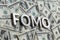 The word FOMO laid with aluminium letters on the US dollar banknotes background - with selective focus