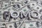 The word FOMO laid with aluminium letters on the US dollar banknotes background - with selective focus