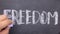 Word FREEDOM, written by hand in chalk on a blackboard.
