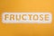 Word Fructose made of sugar on orange background, top view