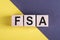 Word FSA - flexible spending account, on wooden cubes on yellow - gray background