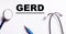 The word GERD is written on a white background near a stethoscope and a marker. Medical concept