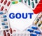 The word GOUT is written on a light background surrounded by multi-colored packages with pills. Medical concept