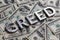 The word GREED laid with aluminium letters on the US dollar banknotes background - with selective focus