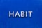 The word habit laid with silver metal characters on blue painted wooden board in central flat lay composition