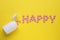 Word Happy made of pink antidepressants and medical bottle on yellow background, flat lay