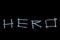 The word hero written with screws on a black background with reflections