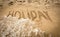 Word Holiday written on sand being washed off by sea wave