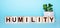 The word HUMILITY is written on wooden cubes near a flower in a pot on a light blue background