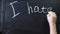 The word `I hate you` written on a black board. The sign is written on a chalk board. Male hand draws in chalk on a