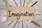 The word imagination painted on wooden board with fanned out paintbrushes behind sign