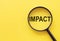 The word IMPACT is written on a magnifying glass on a yellow background
