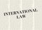 The word INTERNATIONAL LAW written and highlighted in front of blurred text columns on background of light yellow color