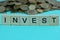 Word invest wooden letters on a green background with a pile of coins