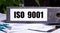 The word ISO 9001 is written on a gray file folder next to documents. Business concept