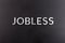 The word jobless laid with white scratched metal letters on flat black surface