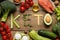 Word Keto made with products surrounded by different food on wooden table, flat lay