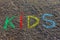 Word KIDS written with colorful crayons on the asphalt, ground.