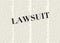 The word LAWSUIT written and highlighted in front of blurred, text columns on background of light yellow color