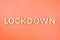 The word lockdown laid with brushed aluminium metal letters on lush lava orange color background