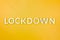 The word lockdown laid with brushed aluminium metal letters on yellow background