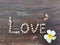 Word love laid out of small sea shells with plumeria flower on dark brown old shabby wooden background with cracks