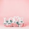 Word LOVE on pastel pink background with lovely roses bunch, front view. Creative female holidays layout