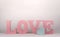 Word love with pink cork letters and a small cardboard box in the shape of a heart on a white background. valentine`s day concept