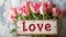 the word "Love" placed next to a beautifully arranged bouquet of tulips on a light background, blending modern