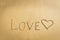 Word Love written on the sand heart drawn message romantic symbol concept