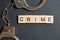 A word made of wooden letters is a crime. Metal handcuffs on a gray background. The concept of breaking the law